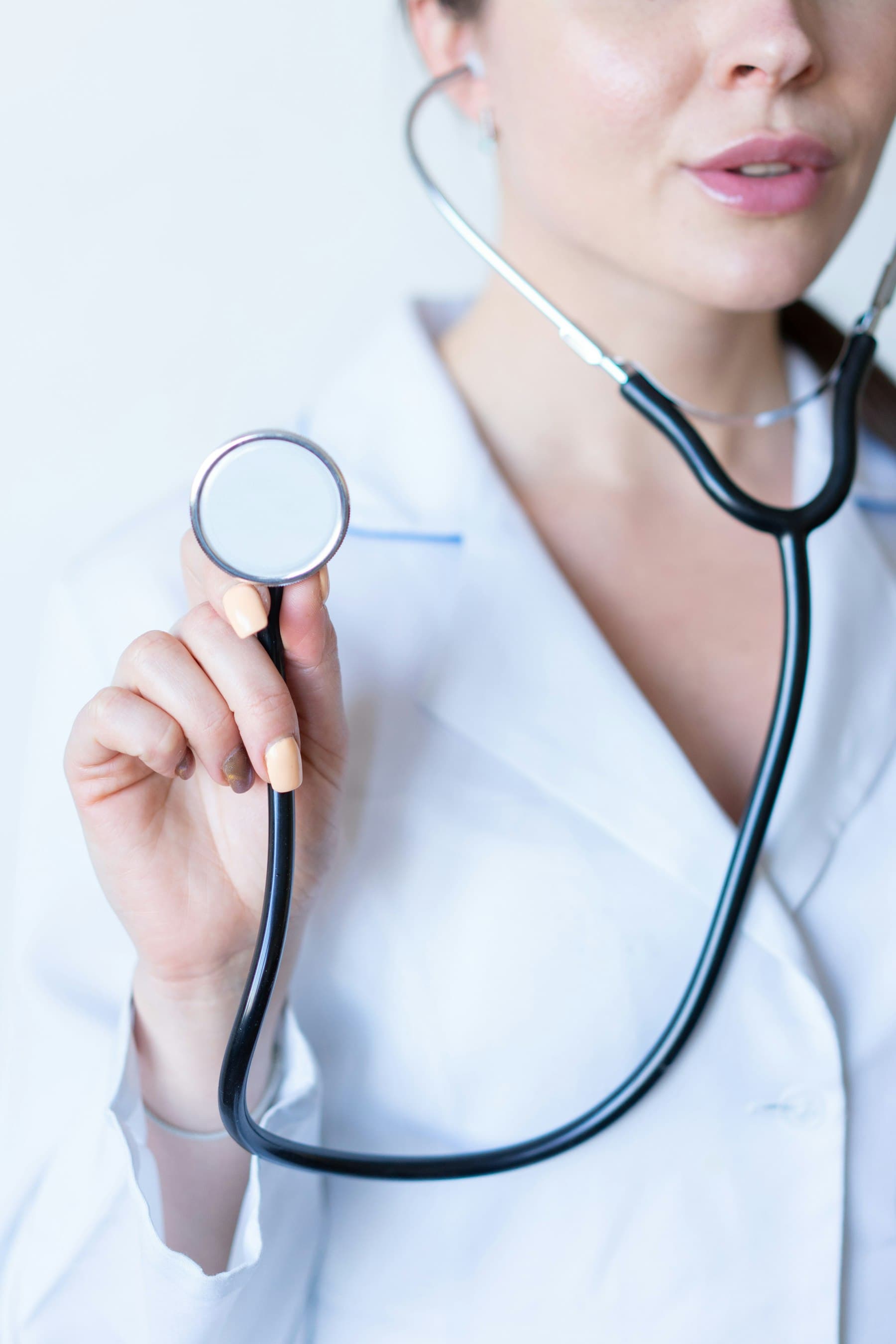 A clinician holding out a stethoscope, white coat behind