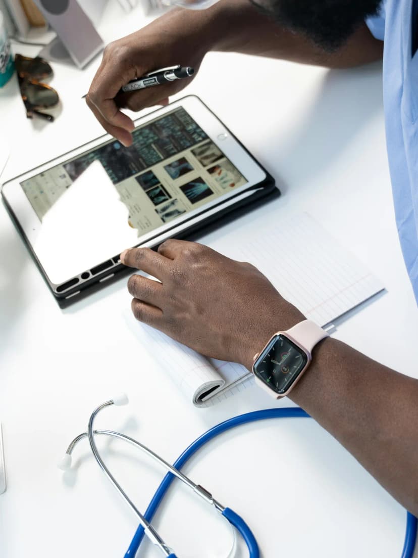 A clinician updating notes on a tablet, stethoscope on the desk
