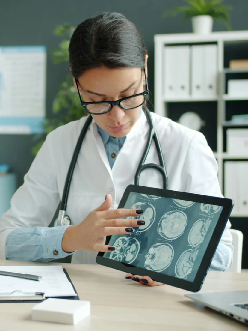 A doctor at her desk reviewing a patient's scans on a tablet